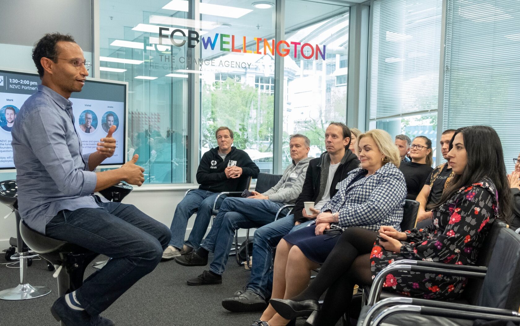 A speaker on a stool addressing a seated audience at FCB Wellington during NZVC Portfolio Day 2022, with the partners’ introduction slide on screen