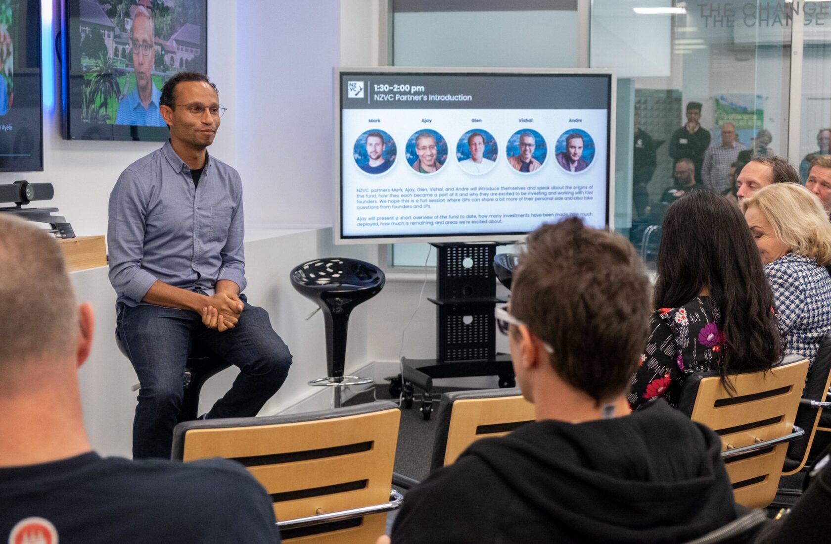 A partner seated on stage beside the slide introducing the NZVC partners at Portfolio Day 2022