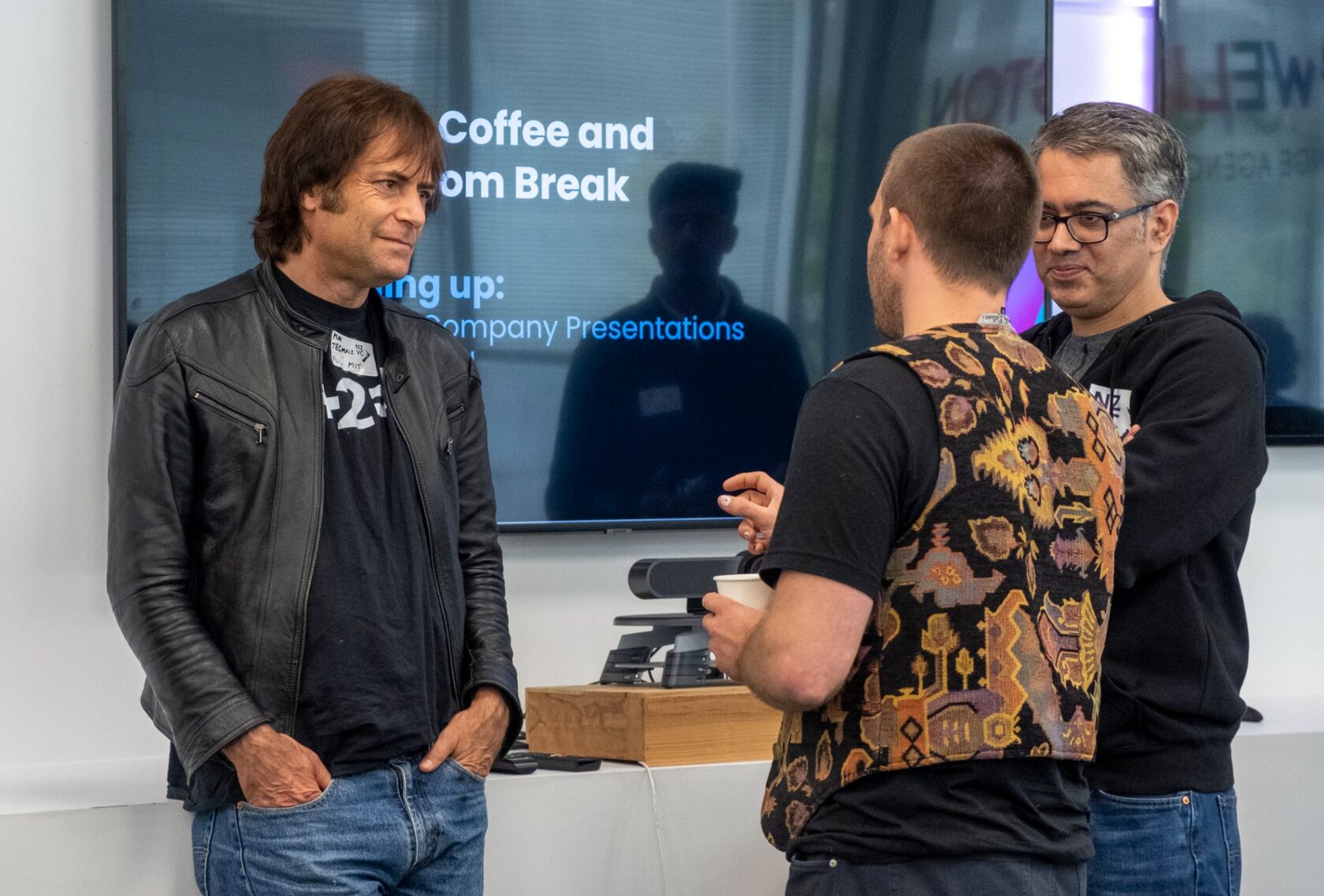 Attendees talking in front of the screen marking the coffee and room break