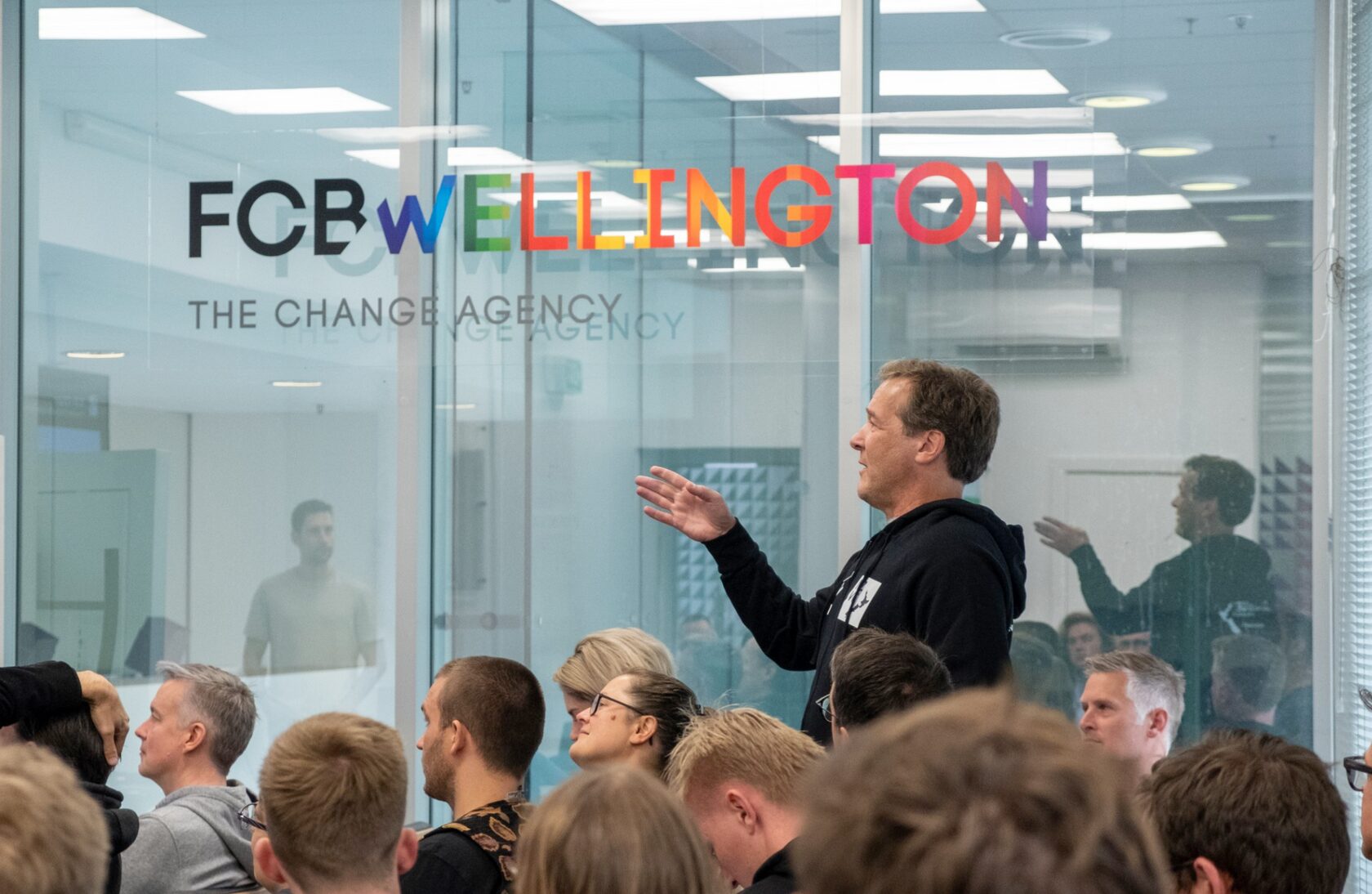 Attendees watching a speaker through the glass wall of the FCB Wellington office