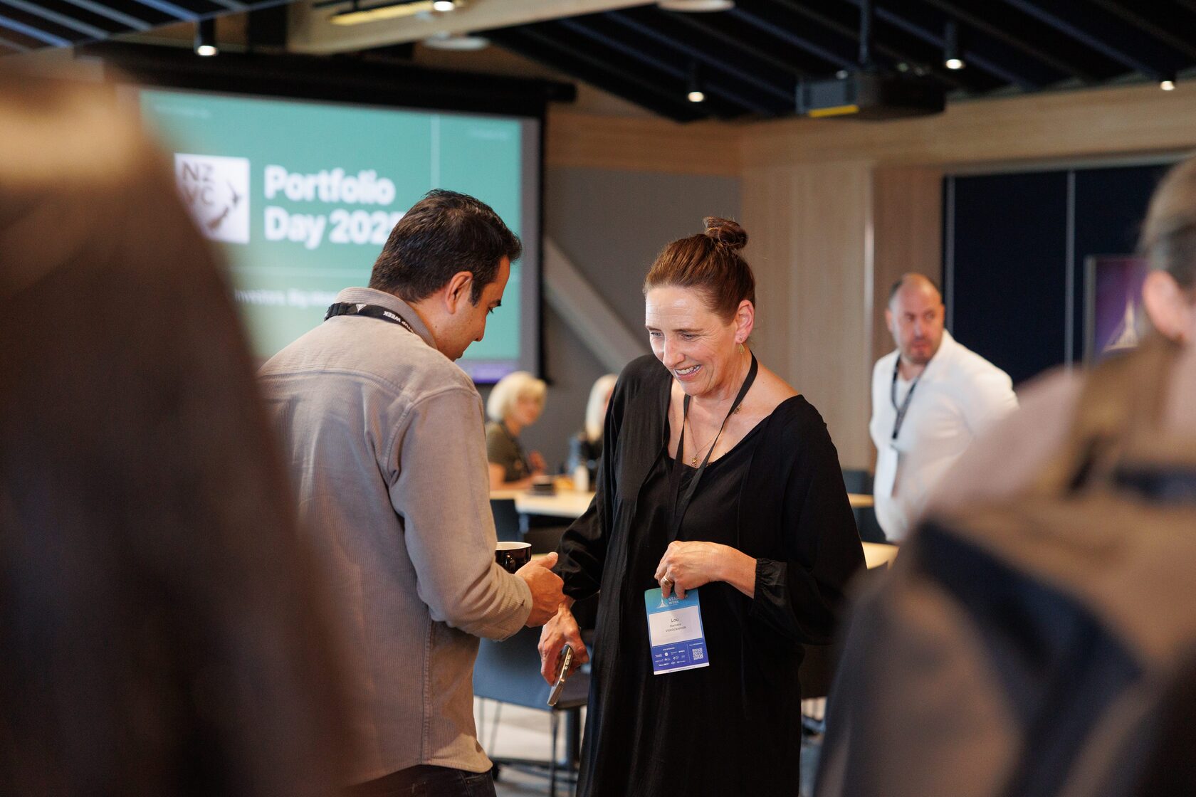 Two attendees shaking hands in front of the Portfolio Day 2025 stage screen