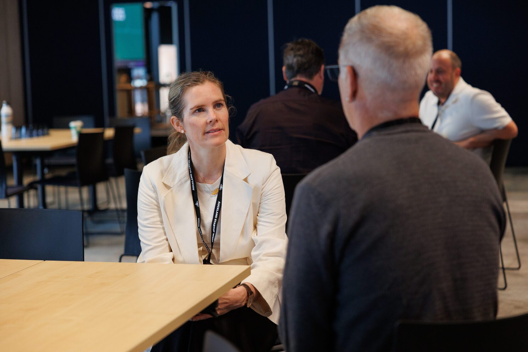 Two attendees seated at a long table in conversation during a break