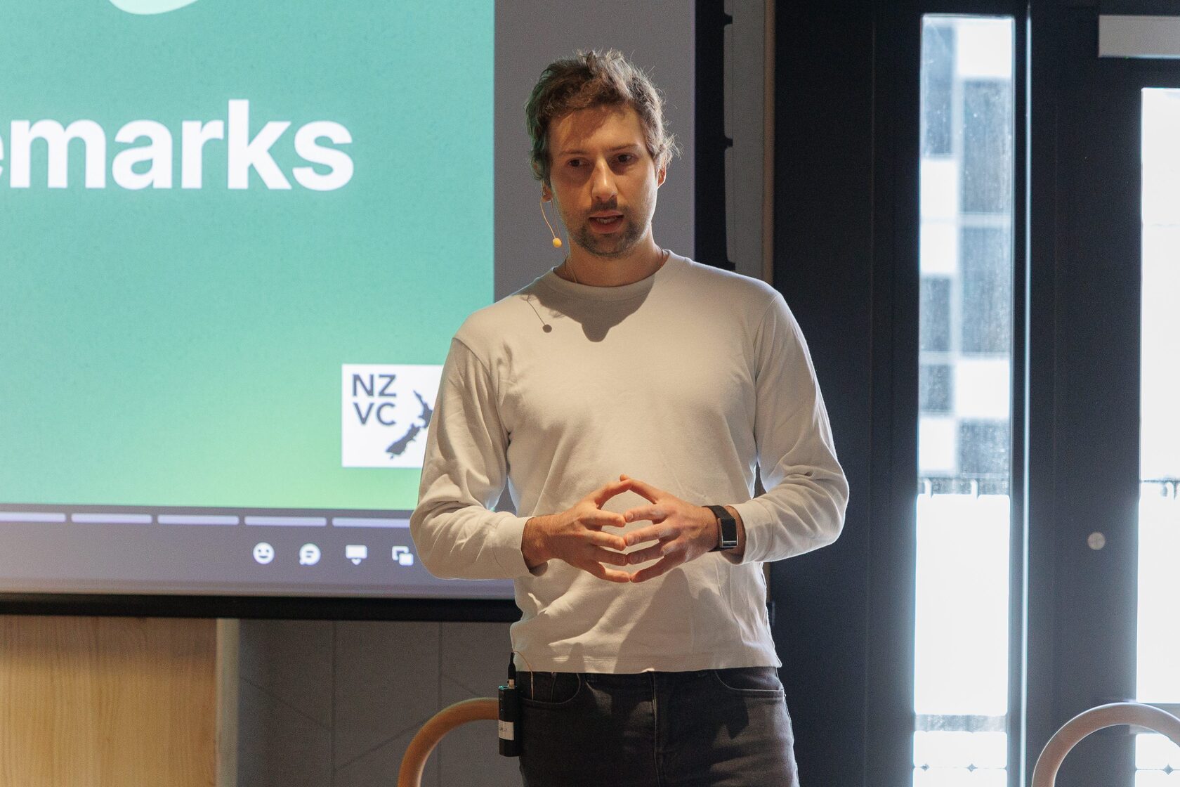 A speaker delivering opening remarks in front of a green NZVC slide at Portfolio Day 2025