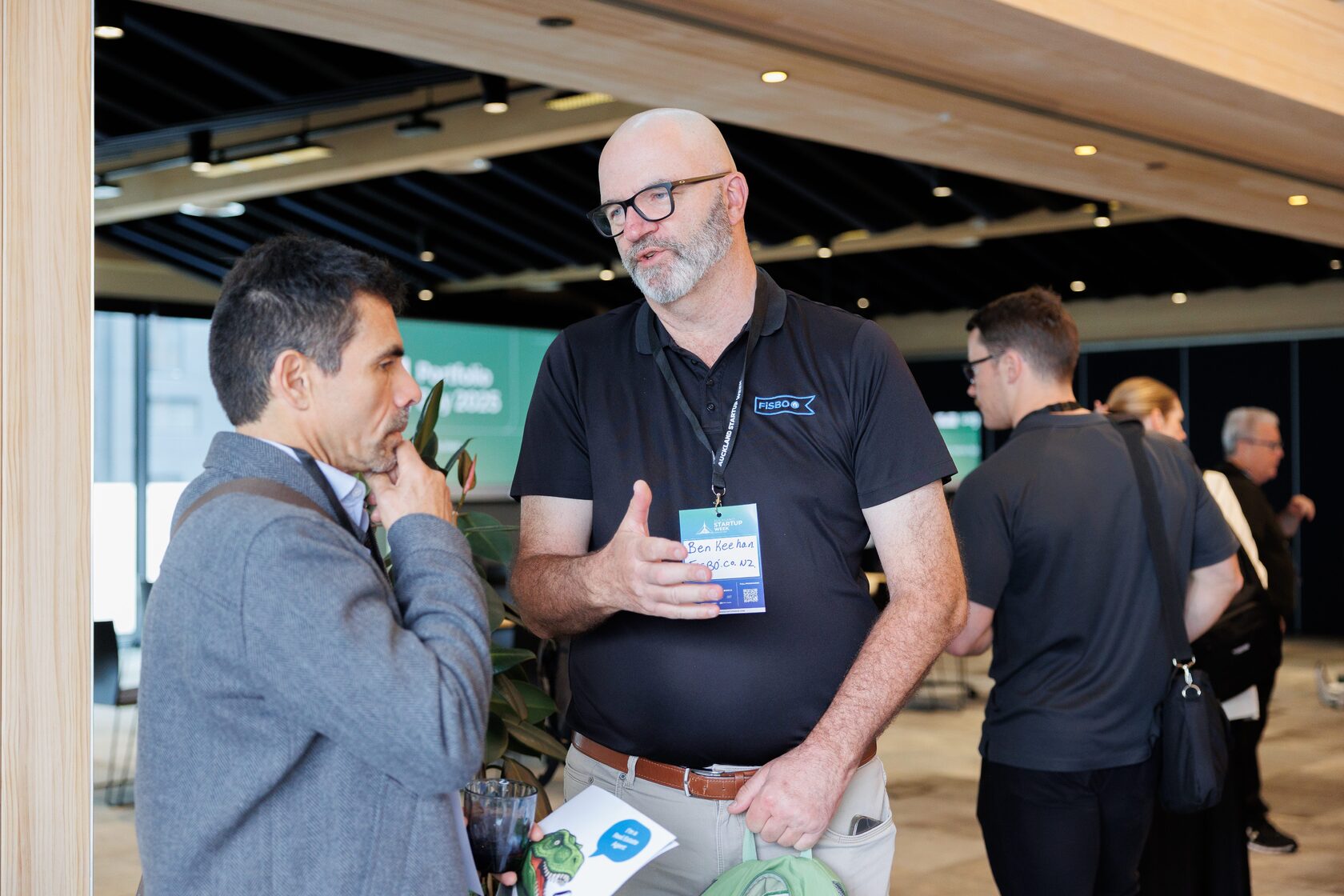 Two attendees deep in conversation in front of the Portfolio Day 2025 welcome screen