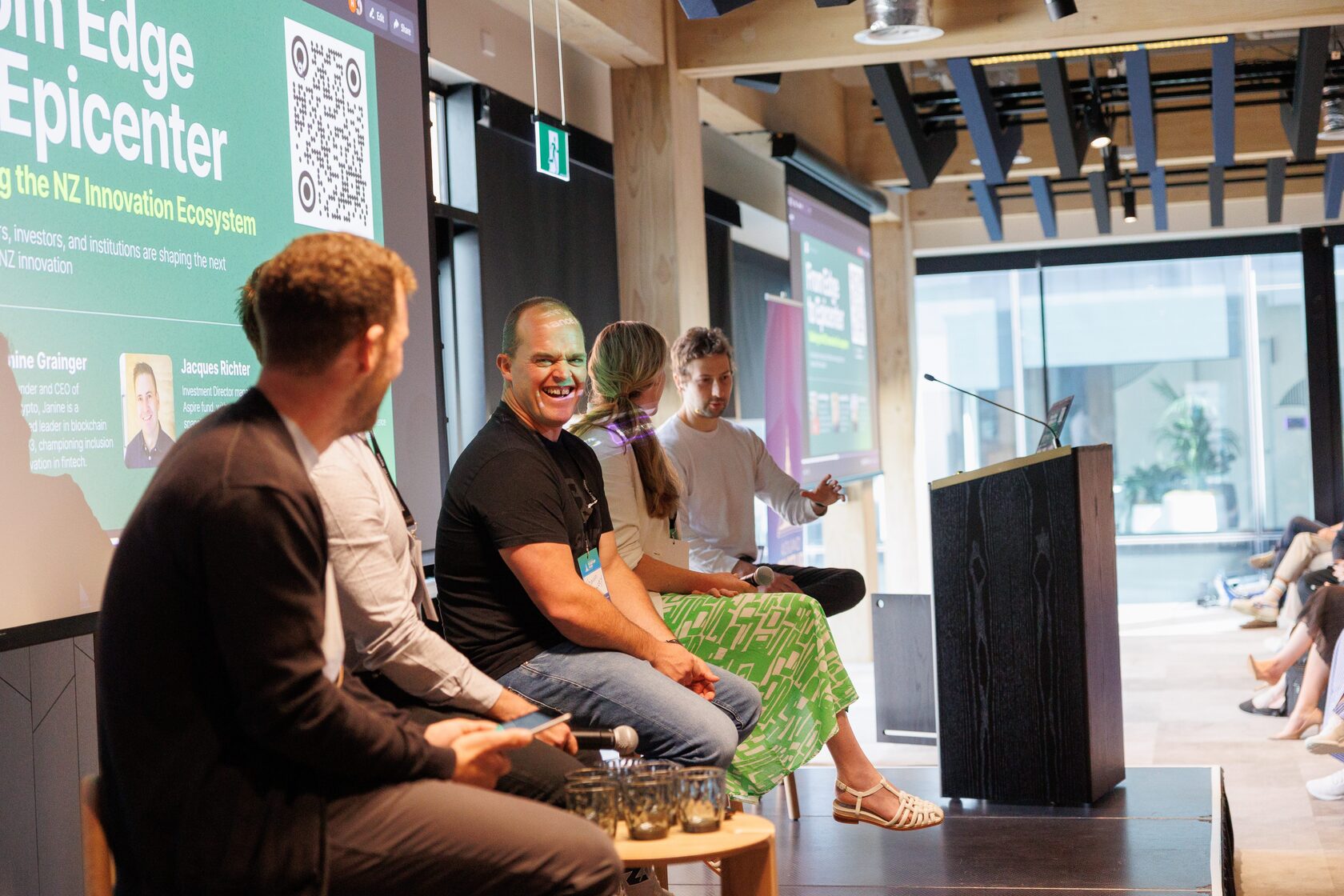 Panelists seated on stage beside a lectern under the From Edge to Epicenter slide