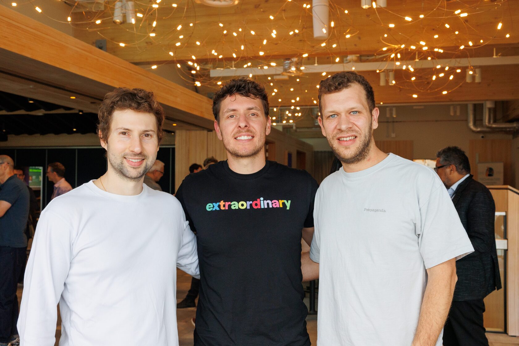 Three founders, two of them in Extraordinary t-shirts, standing together in the foyer