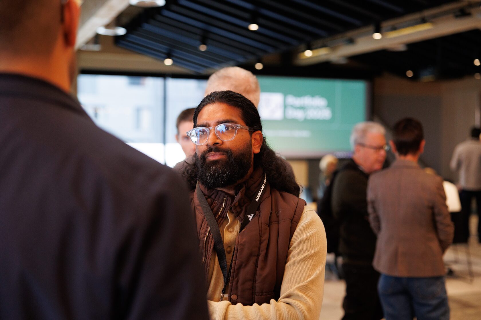 An attendee laughing mid-conversation with the Portfolio Day 2025 screen behind him