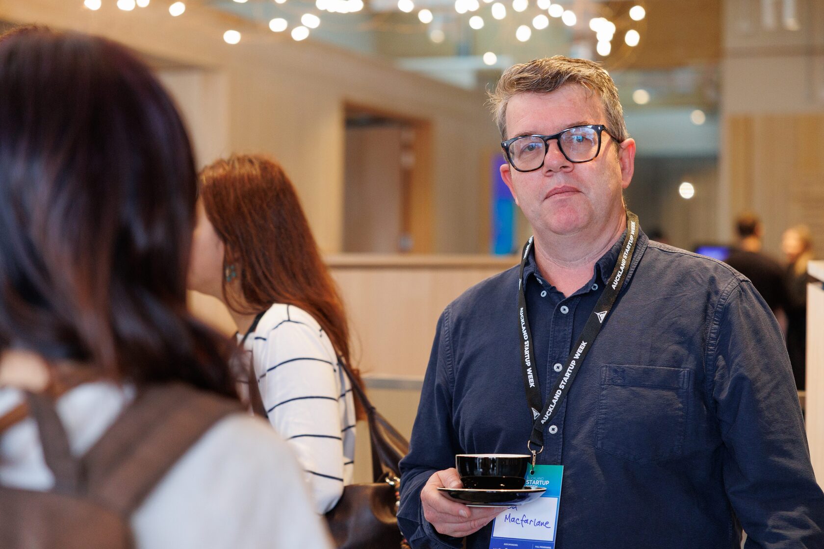 An attendee holding an espresso cup and a conference lanyard during the morning break