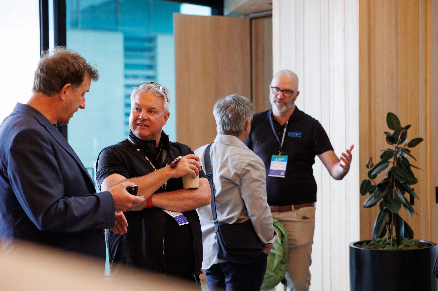 Four attendees in conversation beside a potted plant in the foyer