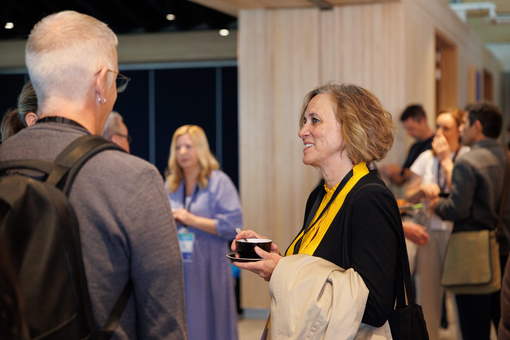 Two attendees greeting each other over coffee near the doors