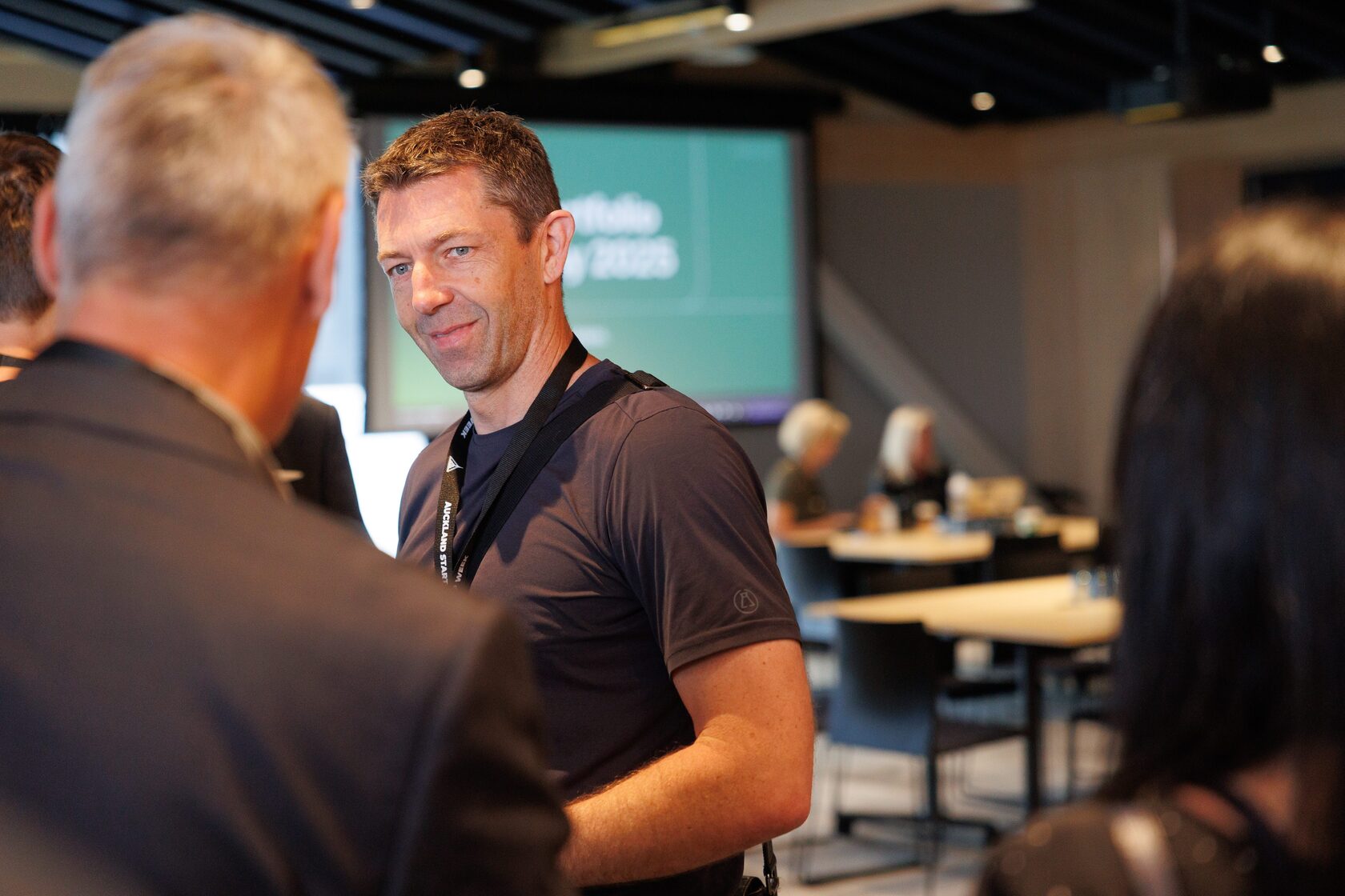 A speaker in conversation with an attendee in front of the Portfolio Day 2025 title screen