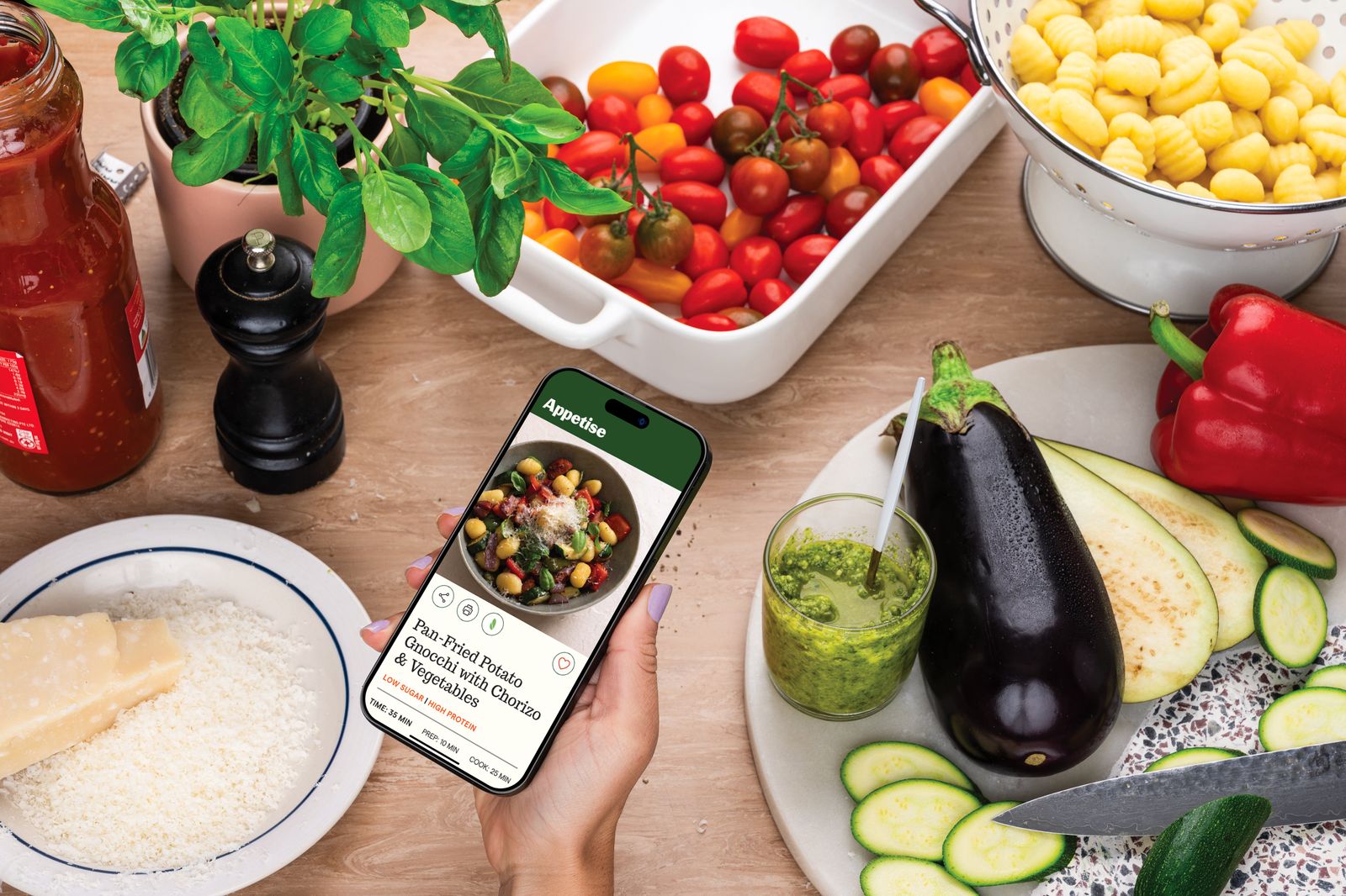 A phone showing an Appetise recipe on a bench with ingredients