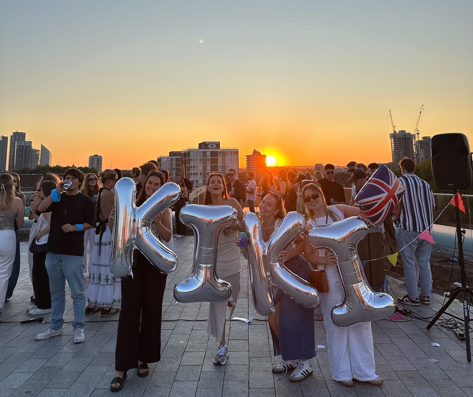 Kiki members hold up inflatable letters spelling the company name at a member event at sunset.