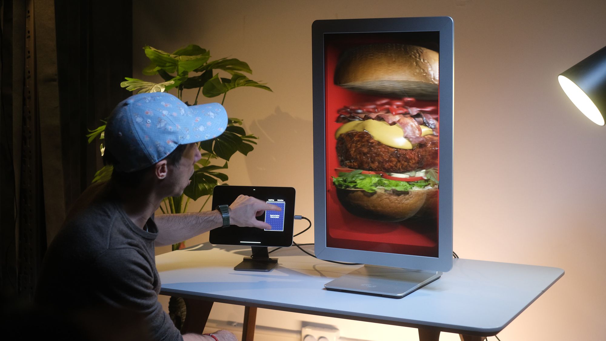 A person works at a desk beside a display holding a burger in three dimensions above the screen.