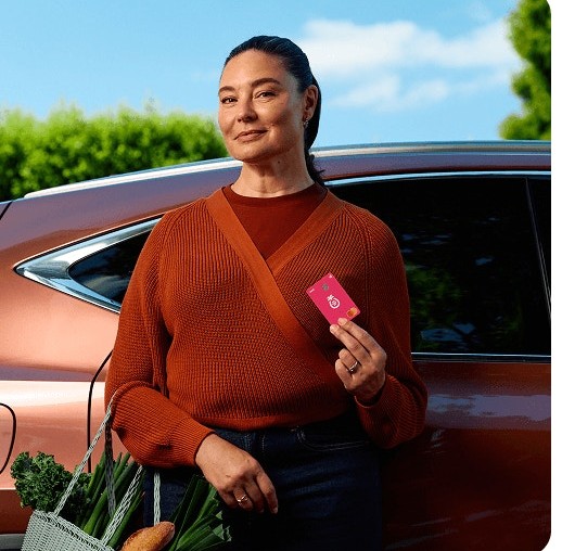 A woman holding a Sharesies card beside her car